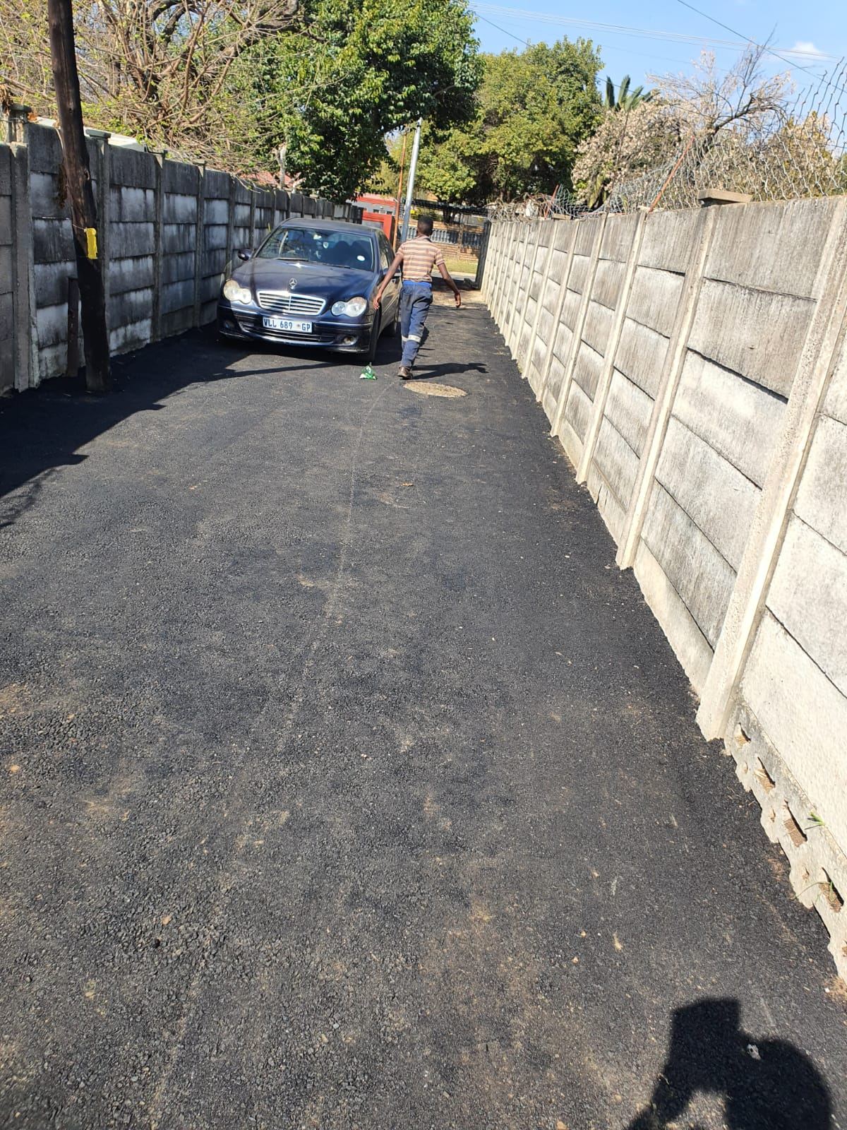 Tar driveway alongside brick wall